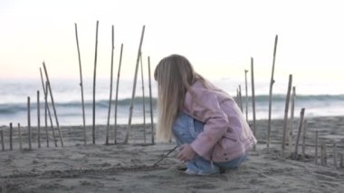 Tetik çeken küçük bir kız ve kotlar akşamları kumsalda sopalarla oynuyor. Bir kız kumsalda kulübe yapıyor, Türkiye, Alanya