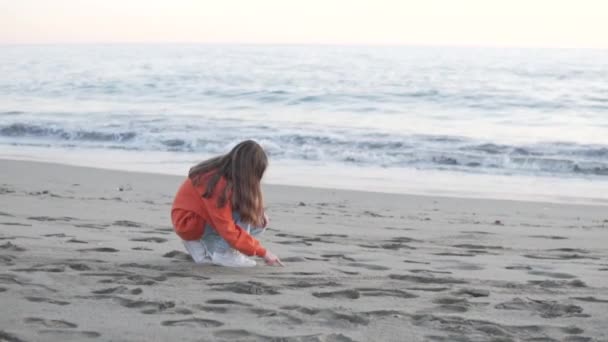 ブルネットの女の子が海によってビーチで砂の上に描画します — ストック動画