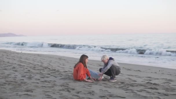 海のそばの砂浜に座って話をしています — ストック動画
