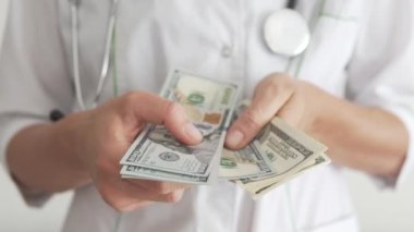 Doktor 100 dolarlık banknotlar halinde parayı sayıyor, tıbbi hizmetleri ödüyor. Estetik ameliyat.