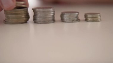 Yakın plan, bir insan parmağı farklı değerlerdeki metal para yığınlarını sayar.