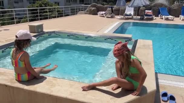 夏天有两个穿着泳衣的女朋友坐在游泳池边 土耳其 阿拉亚 一个炎热的夏天 孩子们在晒日光浴和洗澡 — 图库视频影像
