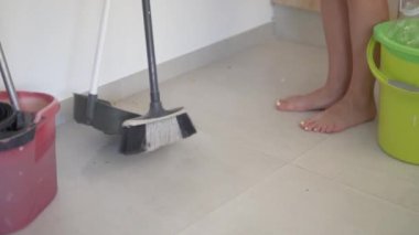 Bir kadın mutfaktaki kirli döşemeleri süpürüyor..