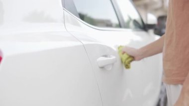 Bir kadın beyaz bir arabanın kirini bez parçasıyla temizliyor. Yakın plan.