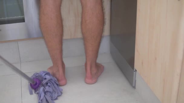 Seorang Pria Mengangkat Kakinya Saat Seorang Wanita Mencuci Lantai Dapur — Stok Video