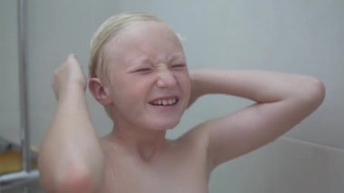 Sarışın çocuk saçlarını şampuanla yıkıyor, çocuğun duş alırken yakın çekimi var..