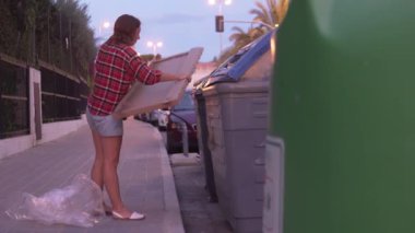 Akşam vakti mobilyaların altından büyük karton kutuları çöp tenekesine atan kadın. Çöp tenekesi, İspanya, Alicante..