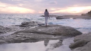 Mutlu bir kadının güzel videosu, deniz boyunca kayalarda yürüyen bir kız. Saten etek rüzgarda gelişir, arkadan manzara. İspanya, Alicante