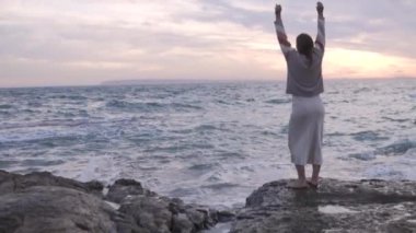Arkadan bak, güzel bir kadın akşam deniz kenarında bir kayanın üzerinde dans ediyor. İspanya, Alicante