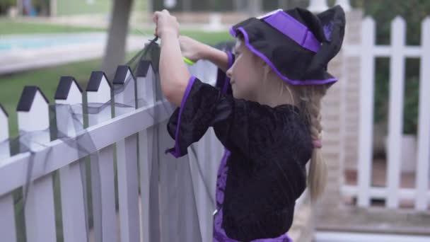 一个穿着巫婆服装的女孩在房子的篱笆上装饰万圣节假期 — 图库视频影像