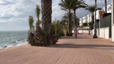 Kasklı bir kız deniz boyunca bisiklet sürüyor. Alicante, İspanya