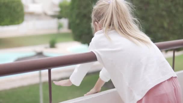 美丽的小女孩站在阳台的阳台上看着花园 侧视图 — 图库视频影像