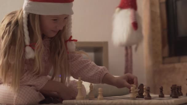 Όμορφο Κοριτσάκι Χριστουγεννιάτικο Καπέλο Και Πιτζάμες Παίζει Σκάκι — Αρχείο Βίντεο