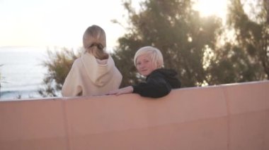 Sarışın çocuk beton bir bankta kız kardeşiyle oturuyor ve parktaki denize bakıyor. İspanya, Alicante