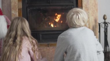 Erkek ve kız kışın şöminenin yanında ısınırlar, çocuklar şöminenin yanında oturur ve ateşe bakarlar. İspanya, Alicante