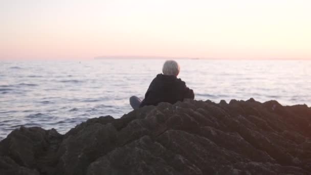 Красивий Блондинка Сидить Скелях Біля Моря Заході Сонця Вид Ззаду — стокове відео