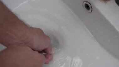 Yakın plan, bir adam lavabodaki tıkanıklığı kabloyla temizlemeye çalışıyor..
