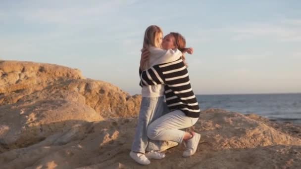ハッピーママは海で岩の上に彼女の小さな金髪の娘を抱きしめました 楽しい — ストック動画