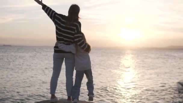 後ろから見ると 小さな娘が日没時に海で岩の上に抱きしめて立っています スペイン アリカンテ 2024 — ストック動画