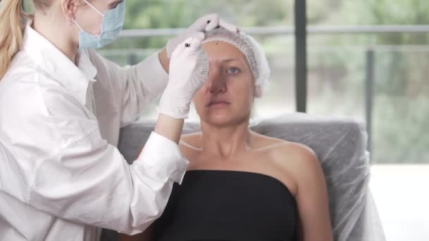 一个女人正在接受肉毒杆菌注射在她的脸上 而她的手轻轻地放在她的大腿上 一个平静的姿态 肉毒杆菌注射前 美容师会在女人脸上做记号 — 图库视频影像
