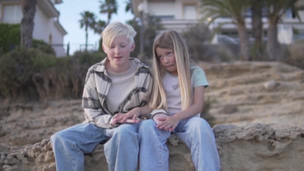 Chłopiec Dziewczynka Siedzą Skalistej Plaży Dzieląc Uśmiech Ciesząc Się Elektrycznym — Wideo stockowe