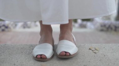 Yerde duran beyaz ayakkabılı bir insanın yakın plan fotoğrafı. Beyaz ayakkabılar asfalt yol yüzeyiyle tezat oluşturuyor, insan bacakları ve ayaklarını vurguluyor.