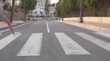 Bir kadın yaya geçidinden karşıya geçerken geniş adımlar atar, yavaş çekim çeker. İspanya, Alicante