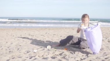 Küçük kız plajdaki çöpleri plastik bir torbayla topluyor. İspanya, Alicante. Çocuk kendinden sonra çöpü temizler..