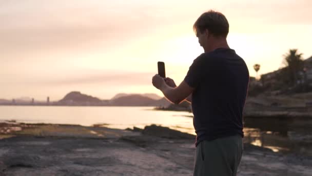 Mężczyzna Robi Zdjęcie Panoramiczne Morza Zachodzie Słońca Przez Telefon Komórkowy — Wideo stockowe