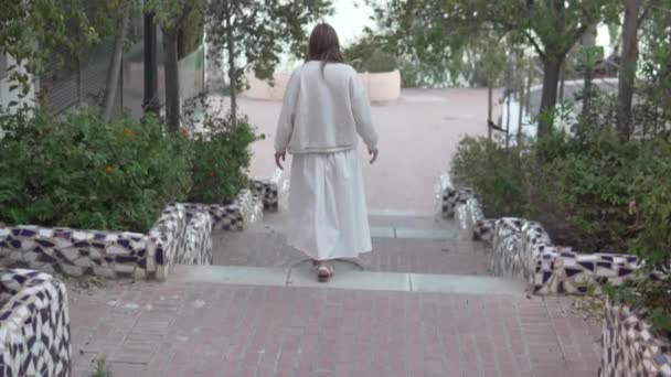 一个穿着白色长裙的女人走在绿树之间的一个公园的台阶上 阿利坎特 德韦尔塔 — 图库视频影像