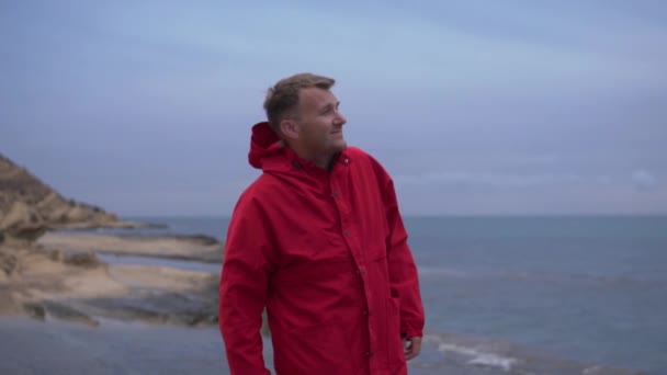 Красива Брюнетка Червоній Куртці Дивиться Розсіяне Небо Скелі Біля Моря — стокове відео