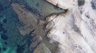 Uçsuz bucaksız sulara bakan kayalık kıyıların ve kayalıkların nefes kesici hava manzarası. Bu video güzelliği ve kıyı manzarasını sergiliyor. Kuadkopter insanın üzerinden uçar.