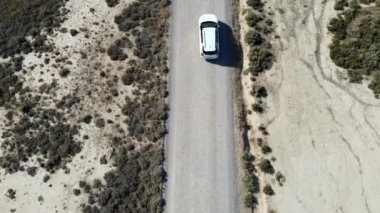 Çöl yolunda beyaz bir araba sürüyor. Uçsuz bucaksız, kurak manzaraların dingin güzelliğini gösteren engebeli çöl arazisinde beyaz bir minibüs ve bir araba.