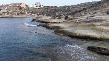 İspanya, Alicante, Cabo de Huertas plajı. Sabahları deniz kenarında egzersiz yapan güzel bir kadın, İHA atışı, güzel kayalık plaj ve deniz..