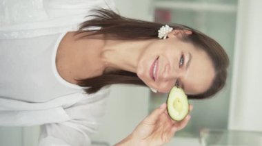 Dikey video. Çekici Avrupalı bir kadının elinde taze avokado tutan portresi ve el bakımı prosedürüyle sınıfı gösteriyor. Güzel kız reklamı. Yüze yakın sağlık kozmetolojisi