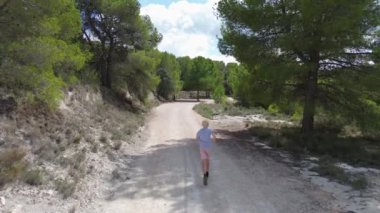 Sarışın bir çocuk dağ orman yolunda koşuyor, arkadan bir drona ateş ediyor. İspanya 'nın güneyi