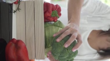 Bir kadın bir kutu çiftlik sebzesi topluyor. Dikey video, yakın plan.