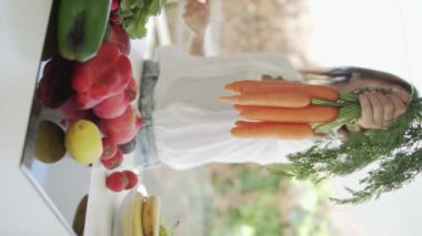 Dikey video, yavaş çekim. Bir kadın beslenme uzmanı kameraya bir demet taze havuç uzatıyor..