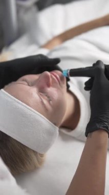 Genç bir kadın kozmetik kliniğinde Hydrafacial prosedüre tabi tutuluyor. Yakın çekim, dikey video.
