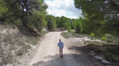 Ormanlık bir arazide sakin bir yolculuk, erkek ve kadınların dolambaçlı toprak bir yol boyunca fiziksel aktivitelerle meşgul olduğu, bereketli doğa ile çevrili