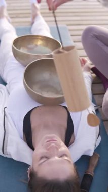 Yoga minderinin üzerinde rahatlatıcı bir kadın sahnesi. Kafasında şarkı söyleyen kâselerle, rahatlatıcı titreşimlere dalıyor, dengeyi ve iç huzuru simgeliyor.