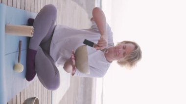 Bir kadın yoga minderinde oturup sakinleştirici bir videoda şarkı söylüyor. Uyumlu sesler farkındalık için sakin bir atmosfer yaratır.