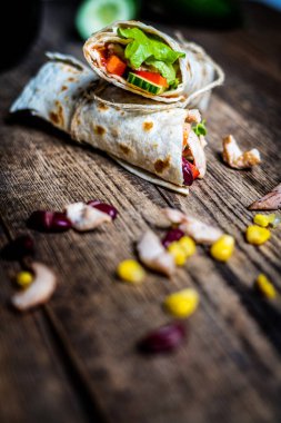 Traditional mexican tortilla wrap with chicken meat and vegetables on wood table