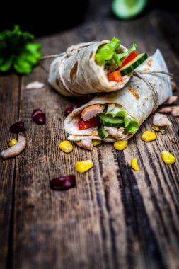 Traditional mexican tortilla wrap with chicken meat and vegetables on wood table