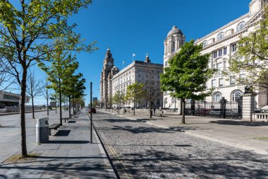 Liverpool Pier Head, with the Royal Liver Building, Cunard Building and Port of Liverpool Building along a roadside, England UK