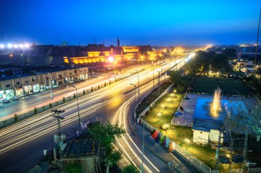 PESHAWAR, PAKISTAN-MAY 06, 2016-Lights trails from moving cars on the evening highway with a group of  buildings and shops on the opposite side.