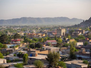 Pakistan 'da dağların yakınındaki küçük bir kasabanın manzaralı panoramik manzarası, sergilenen konut binaları, yemyeşil alanlar ve Mingora şehrinin sakin bir ortamı..