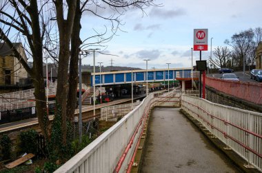Brighouse İstasyonu 'nun yer aldığı şehir demiryolu sahnesinde yaya erişimi ve platform manzarası gösteriliyor. İngiltere 'nin Brighouse şehrinde, Batı Yorkshire' da kırsal bir ortamda kırsal mimari ile çevrili.