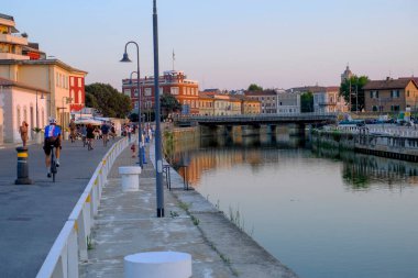 June 2022 Senigallia, Italy: View of the canal and the bridge during the sunset over the city line. Urban view. City postcard clipart