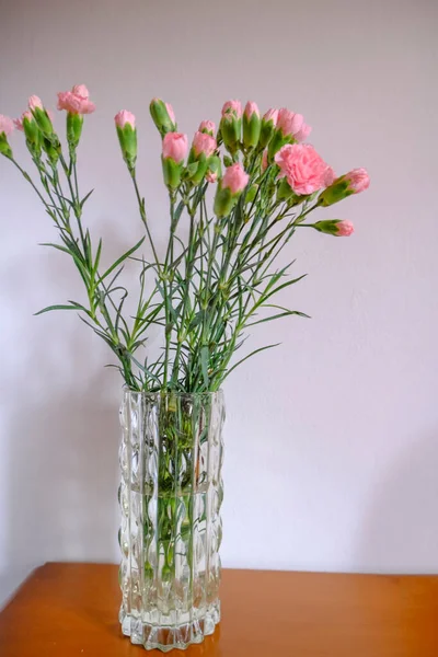 一束粉红色的康乃馨在一个水晶花瓶里 穿过木制抽屉上的白墙 复制空间 家居装饰 — 图库照片
